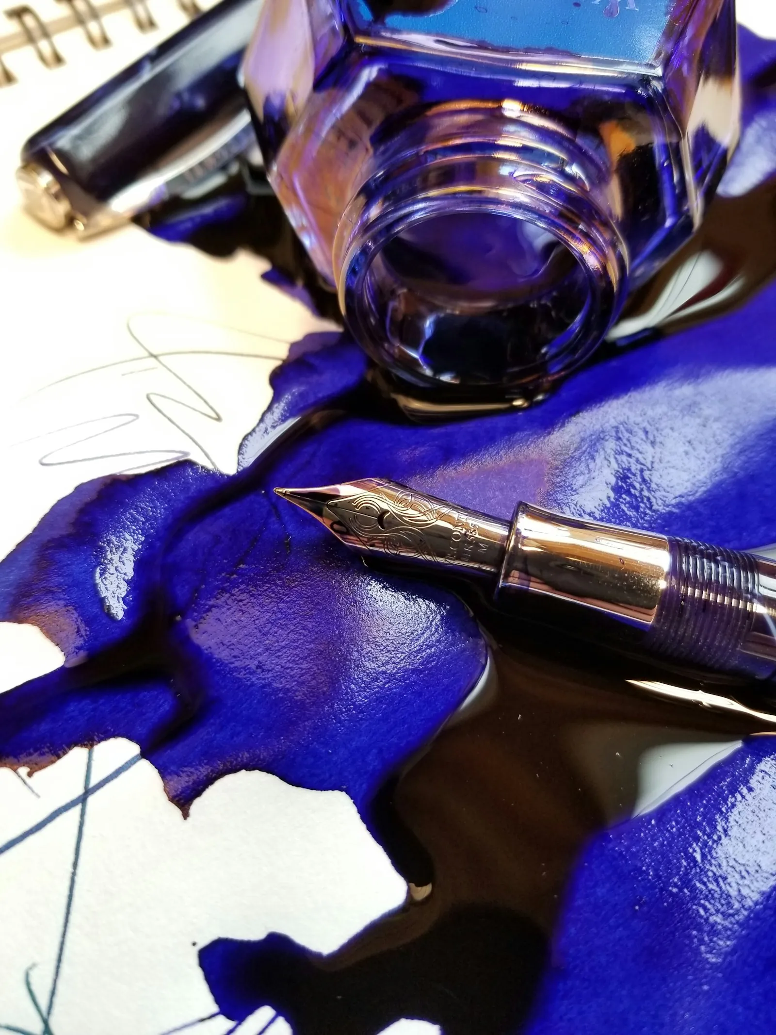 Blue ink spilled around a fountain pen and open ink bottle