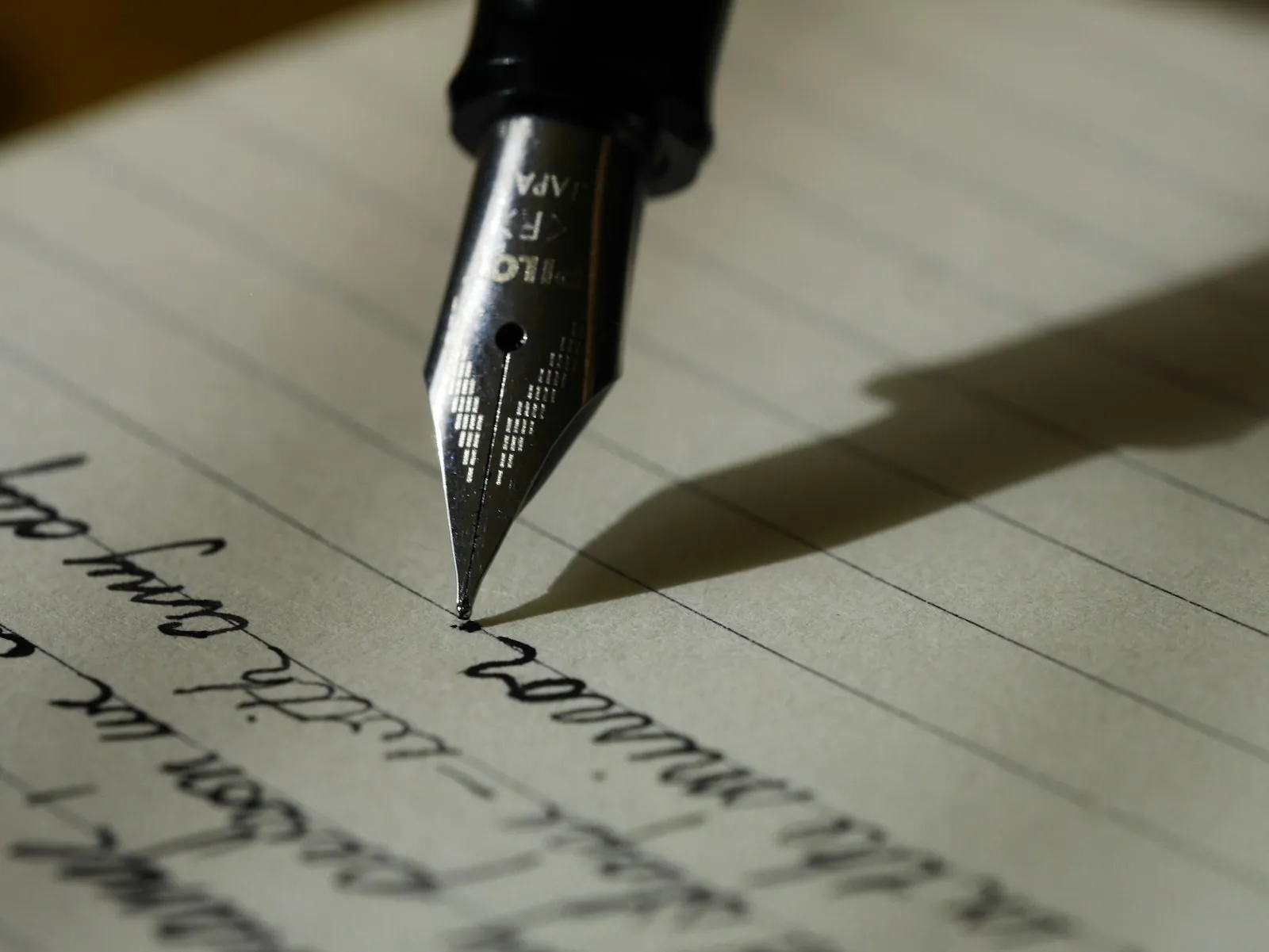 A close-up of a fountain pen nib with ink visible at the tip, resting on a notebook page